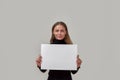 Portrait of lovely young caucasian woman smiling at camera, holding white blank banner in front of her while standing Royalty Free Stock Photo