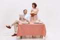 Portrait of loving couple, man reading newspaper, woman serving table, having breakfast  on white background Royalty Free Stock Photo