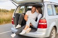 Portrait of loving couple sitting in car trunk wearing white shirts traveling together, talking and smiling, being fall in love, Royalty Free Stock Photo