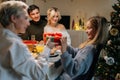 Portrait of loving grandmother giving festive box with Christmas present to adorable granddaughter sitting at dinner Royalty Free Stock Photo