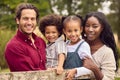 Portrait Of Loving Mixed Race Family Leaning On Fence On Walk In Countryside