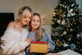 Portrait of loving mother embracing adorable little daughter after giving Christmas present to adorable daughter sitting Royalty Free Stock Photo