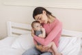 Portrait of loving mother resting with her infant baby girl in bed, woman holding daughter on hands and cuddling Royalty Free Stock Photo