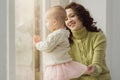 A portrait of a loving mother who plays with her baby while sitting by the window. A beautiful young woman admires the Royalty Free Stock Photo