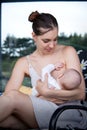 Portrait of loving pretty mom breastfeeding infant in front of grey glass window