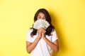 Portrait of lucky african-american girl winning money prize, holding cash and looking amazed, standing over yellow Royalty Free Stock Photo