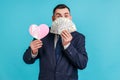 Portrait of lucky rich bearded man in official style suit hiding half of face with dollar banknotes and holding pink paper heart, Royalty Free Stock Photo