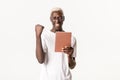 Portrait of lucky winning african-american guy, wearing glasses, holding digital tablet and make fist pump in rejoice