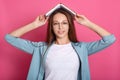 Portrait of magnetic good looking cute young female looking directly at camera, putting opened book on head, having playful mood, Royalty Free Stock Photo