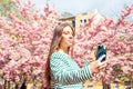 Portrait making selfie female on smartphone on cherry blossom sakura tree. Young smiling caucasian woman is taking selfie portrait