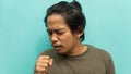 A portrait of a Malay man covering his mouth during coughing on isolated blue background