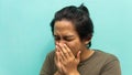 A portrait of a Malay man covering his mouth during coughing and sneezing with isolated blue background