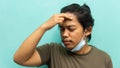 A portrait of a Malay man holding his head, having a headache with painful face reaction on isolated blue background