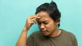 A portrait of a Malay man holding his head, having a headache with painful face reaction on isolated blue background