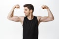 Portrait of male athlete, smiling sportsman flexing biceps, looking pleased at muscle biceps, workout in gym, standing