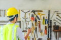 Portrait of a male construction worker in the helmet choosing the many different rusty old tools hanging on a wall Royalty Free Stock Photo