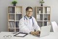 Portrait of male doctor sitting in front of laptop in his bright office of modern clinic. Royalty Free Stock Photo