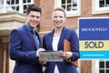 Portrait Of Male And Female Realtors Standing Outside Residential Property