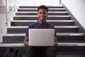 Portrait Of Male High School Student Sitting On Staircase And Using Laptop