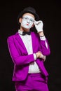 Portrait of male mime artist, isolated on black background. Young man in purple suit is touching his chin with a Royalty Free Stock Photo