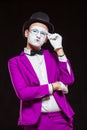 Portrait of male mime artist, isolated on black background. Young man in purple suit is touching his chin with a Royalty Free Stock Photo