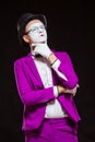 Portrait of male mime artist, isolated on black background. Young man in purple suit is touching his chin with a Royalty Free Stock Photo