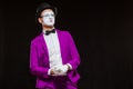 Portrait of male mime artist, isolated on black background. Young man in purple suit is touching his chin with a Royalty Free Stock Photo