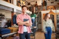 Portrait Of Male Owner Of Fashion Store With Digital Tablet In Busy Clothing Store With Customers