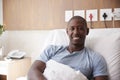 Portrait Of Male Patient Lying In Hospital Bed Smiling At Camera