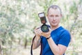 Portrait of male photographer with a DSLR camera in hands, wearing blue t-shirt outdoors on Summer day. Close-up portrait with cop