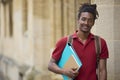 Portrait Of Smiling Male Student Carrying Files Outside University Building In Oxford UK