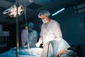 Portrait of male surgeon and African female nurse performing operation under electric lamp in dark modern operation