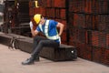 Portrait of a male worker wearing a safety vest and helmet sitting on a steels pallet due to back pain from working Royalty Free Stock Photo