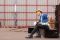 Portrait of a male worker wearing a safety vest and helmet sitting on a steels pallet due to back pain from working Royalty Free Stock Photo