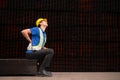 Portrait of a male worker wearing a safety vest and helmet sitting on a steels pallet due to back pain Royalty Free Stock Photo