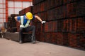 Portrait of a male worker wearing a safety vest and helmet sitting on a steels pallet due to back pain Royalty Free Stock Photo