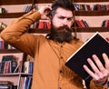 Portrait of man with beard and good eyes reading book in hand on bookshelf background. Education and science concept