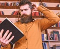 Portrait of man with beard and good eyes reading book in hand on bookshelf background. Education and science concept