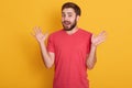 Portrait of man being surprised, handsome male spreading his hands up, posing isolated over yellow background, attractive unshaven