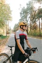 Portrait of man in bicycle outfit standing with bicycle on road in autumn forest on sunset background and resting. Professional