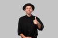 Portrait of a man in a black shirt and pork pie hat holding thumb up isolated over grey background Royalty Free Stock Photo