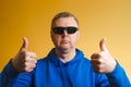 Portrait of a man in a blue hoodie and sunglasses. A man shows a thumbs up gesture on both hands. Royalty Free Stock Photo