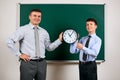 Portrait of a man and boy dressed in a business suits near blackboard background, they show clock - learning and education concept Royalty Free Stock Photo