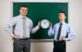 Portrait of a man and boy dressed in a business suits near blackboard background, they show clock - learning and education concept Royalty Free Stock Photo