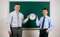 Portrait of a man and boy dressed in a business suits near blackboard background, they show clock - learning and education concept Royalty Free Stock Photo