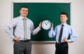 Portrait of a man and boy dressed in a business suits near blackboard background, they show clock - learning and education concept Royalty Free Stock Photo