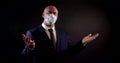 Portrait of a man in a business suit on a black background. he wears a disposable mask, gestures with his hands, speaks