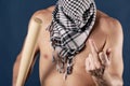 Portrait of a shirtless man in checkered scarf holding a baseball bat and shows finger on blue background Royalty Free Stock Photo