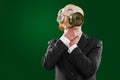 Portrait of a man choking himself wearing a dark business suit and a gas mask, isolated on green background