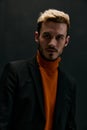 portrait of a man in a coat and an orange sweater blond dark background close-up